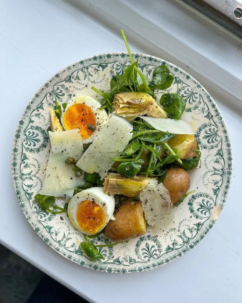 Ensalada primaveral con huevo cocido, papas, queso y vegetales frescos sobre un plato decorado.