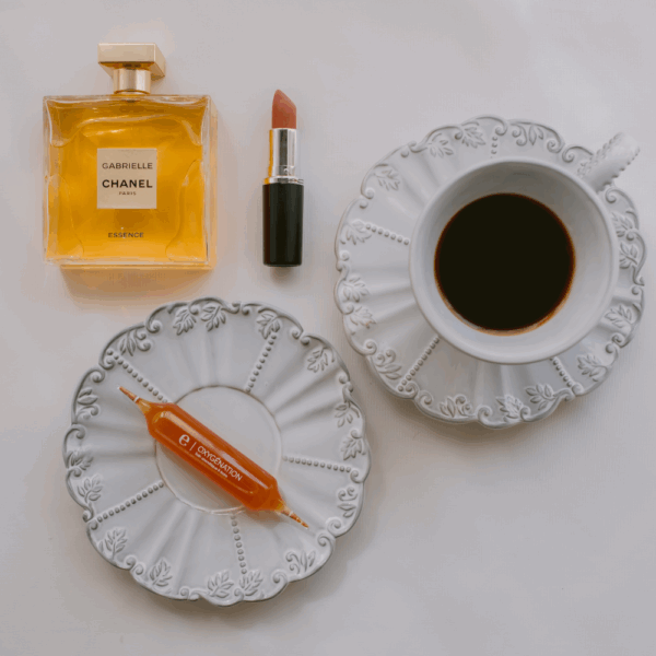 Frasco de perfume Chanel, labial, taza de café y ampolla de complementos alimenticios evoleum Oxygénation sobre un fondo blanco.